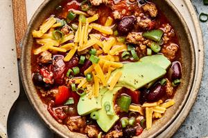 a bowl of homemade turkey chili topped with shredded cheese, avocado and green onions
