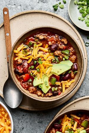 a bowl of homemade turkey chili topped with shredded cheese, avocado and green onions