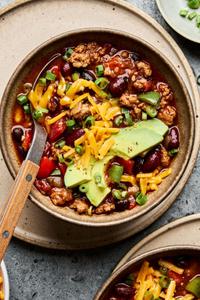 a bowl of homemade turkey chili topped with shredded cheese, avocado and green onions