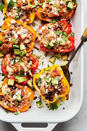 baking dish filled with ground turkey stuffed peppers topped with melted cheese, avocado, cilantro being served with a spoon