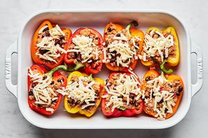 bell pepper halves in a baking dish being filled with ground turkey, cheese, beans and quinoa, topped with shredded cheese