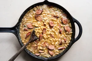 White Bean Sausage Skillet dinner with garlic and chicken stock being stirred together.