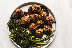 homemade baked teriyaki meatballs being served with roasted broccoli on a plate and drizzled with homemade teriyaki sauce