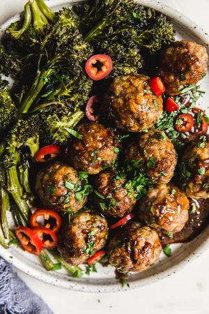 homemade baked teriyaki meatballs with roasted broccoli on a plate, drizzled with teriyaki sauce