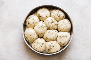 herb and butter rhodes dinner rolls rising in a pan, ready for the oven.