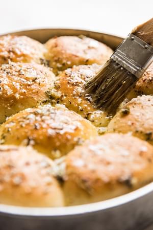pastry brush brushing butter on garlic herb rolls