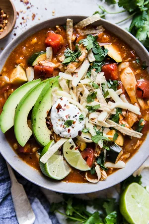 chicken tortilla soup with topped with sour cream avocado and tortilla strips and lime in a bowl