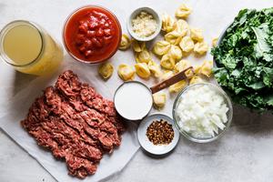 ingredients for creamy tortellini soup: Italian sausage, kale, crushed tomatoes, chicken stock and Parmesan in small bowls