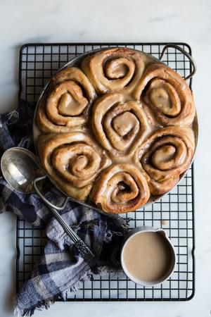 a pan of homemade cinnamon rolls with maple frosting on a baking rack