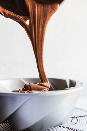 chocolate cake batter being poured into a bundt pan