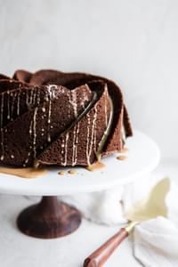 Irish Cream Chocolate Bundt Cake on a cake stand with a linen and serving spoon.