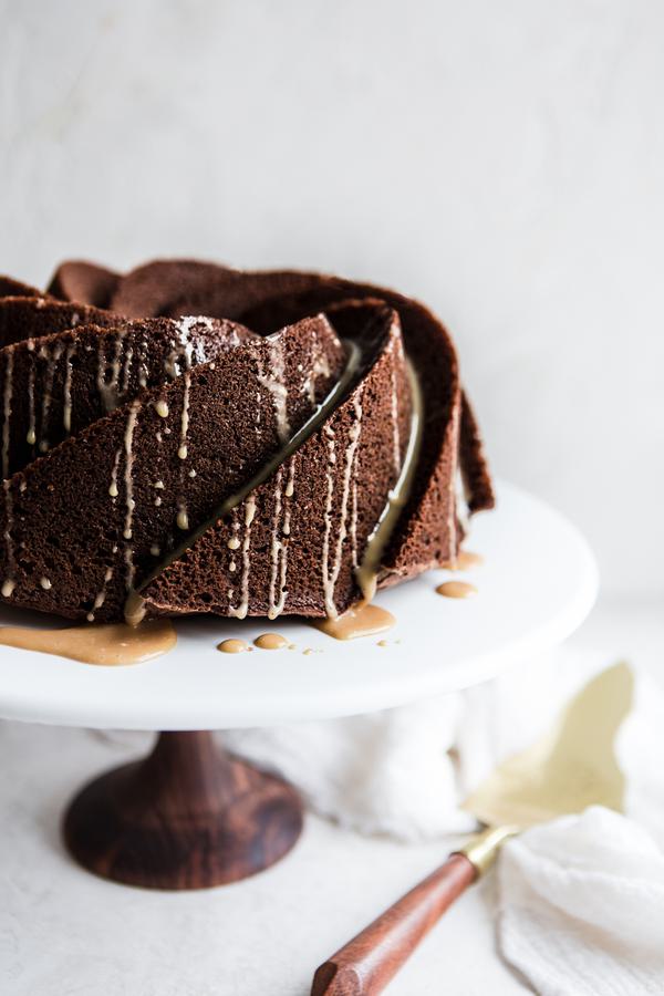 Irish Cream Chocolate Bundt Cake on a cake stand with a linen and serving spoon.