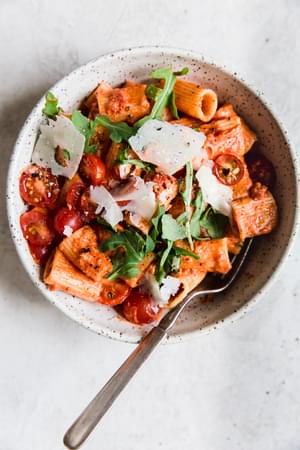 pasta dish with tomato cream sauce arugula and parmesan in a bowl