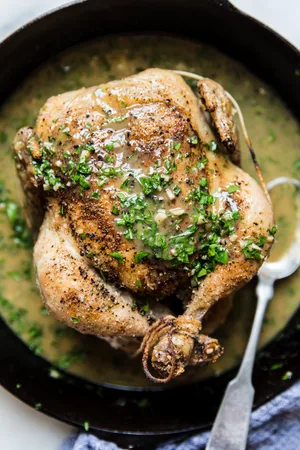 cast iron skillet with whole roasted chicken topped with butter and lemon pan sauce