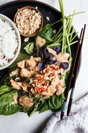 Slow Cooker Swimming Rama over spinach and peanuts on a plate with white rice and chop sticks