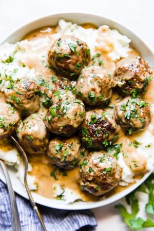 Easy swedish meatballs on a plate of mashed potatoes covered in creamy gravy and sprinkled with fresh parsley.