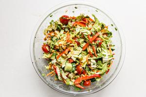 ingredients for Asian chopped salad tossed together in a large glass bowl with Thai peanut dressing