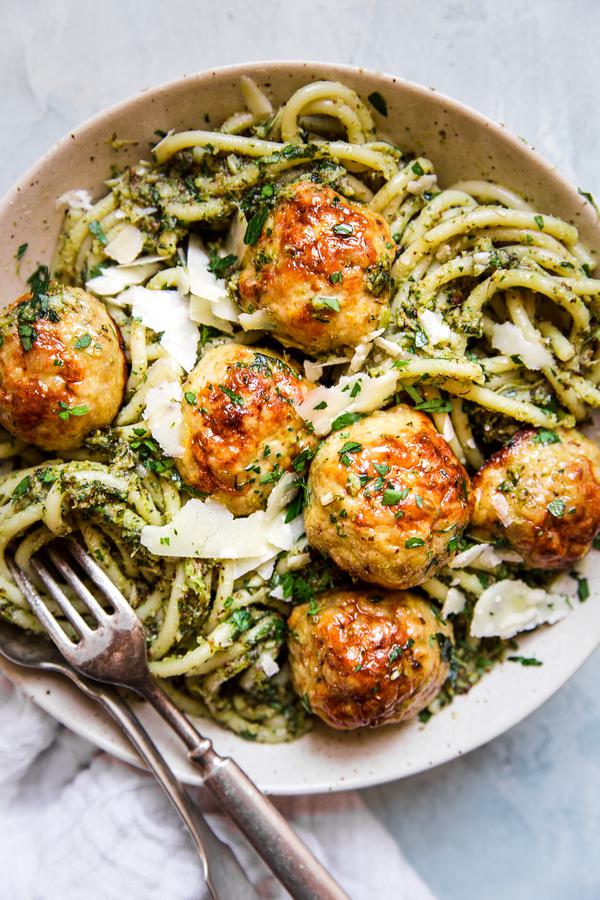 glass bowl of baked chicken meatballs with broccoli pesto pasta topped with parmesan cheese
