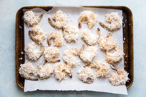 baking sheet of raw shrimp coated in beaten egg, coconut flakes and almond flour