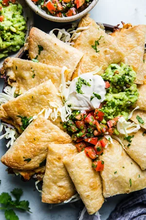 baked chicken quesadillas served with guacamole, fresh pico de Gallo, sour cream and guacamole on a plate