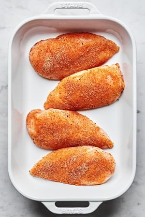 raw chicken seasoned with salt, pepper, garlic powder, onion powder, paprika & brown sugar in a baking dish