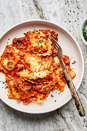 a plate of baked ravioli made with italian sausage, onion, garlic, marinara, spices, cream and mozzarella topped with parsley