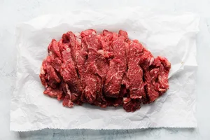 thinly sliced raw steak on parchment paper to be used to make creamy, cozy beef stroganoff