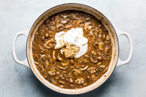 sour cream and dijon being added to mushroom sauce in a skillet to give it a beautiful creamy texture