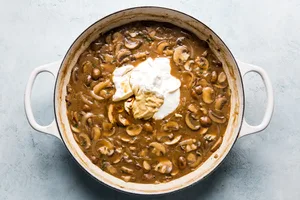 sour cream and dijon being added to mushroom sauce in a skillet to give it a beautiful creamy texture