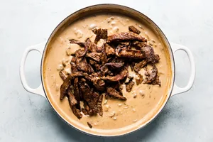 cooked steak being added to beef stroganoff sauce in a large skillet to complete the homemade beef stroganoff