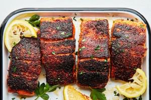 homemade blackened salmon on a serving platter with lemon wedges and sprinkled with fresh parsley