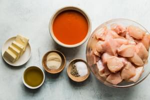bite size chicken breast, buffalo sauce in a bowl, salt, pepper, garlic powder, onion powder, butter and olive oil in bowls