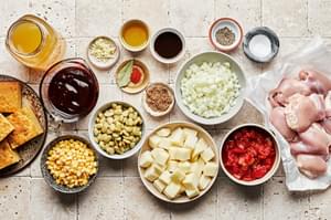 ingredients for Brunswick stew in bowls including spices, corn, lima beans, chicken thighs, potatoes and canned tomatoes