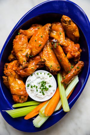Plate of baked buffalo chicken wings served with fresh celery sticks, carrot sticks, and blue cheese dressing for dipping