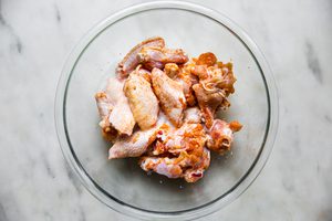 chicken wings tossed in salt, garlic powder, paprika and egg whites in a glass bowl on the counter for baked buffalo wings