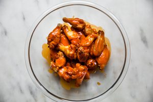 baked seasoned chicken wings being tossed with homemade buffalo sauce