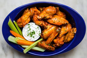 Plate of baked buffalo chicken wings served with fresh celery sticks, carrot sticks, and blue cheese dressing for dipping