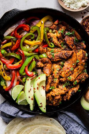 chicken fajitas in a cast iron skillet with bell peppers, avocado, and fresh limes