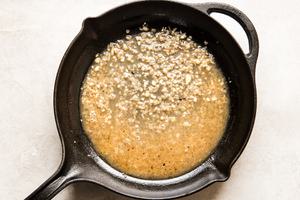shallot, garlic and chicken stock simmering in chicken pan drippings in a cast iron skillet