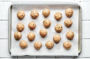 raw homemade chicken meatballs on a parchment lined baking sheet