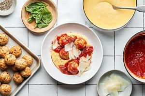 homemade chicken meatballs with polenta and marinara in a bowl surrounded by bowls of more meatballs, polenta, and marinara
