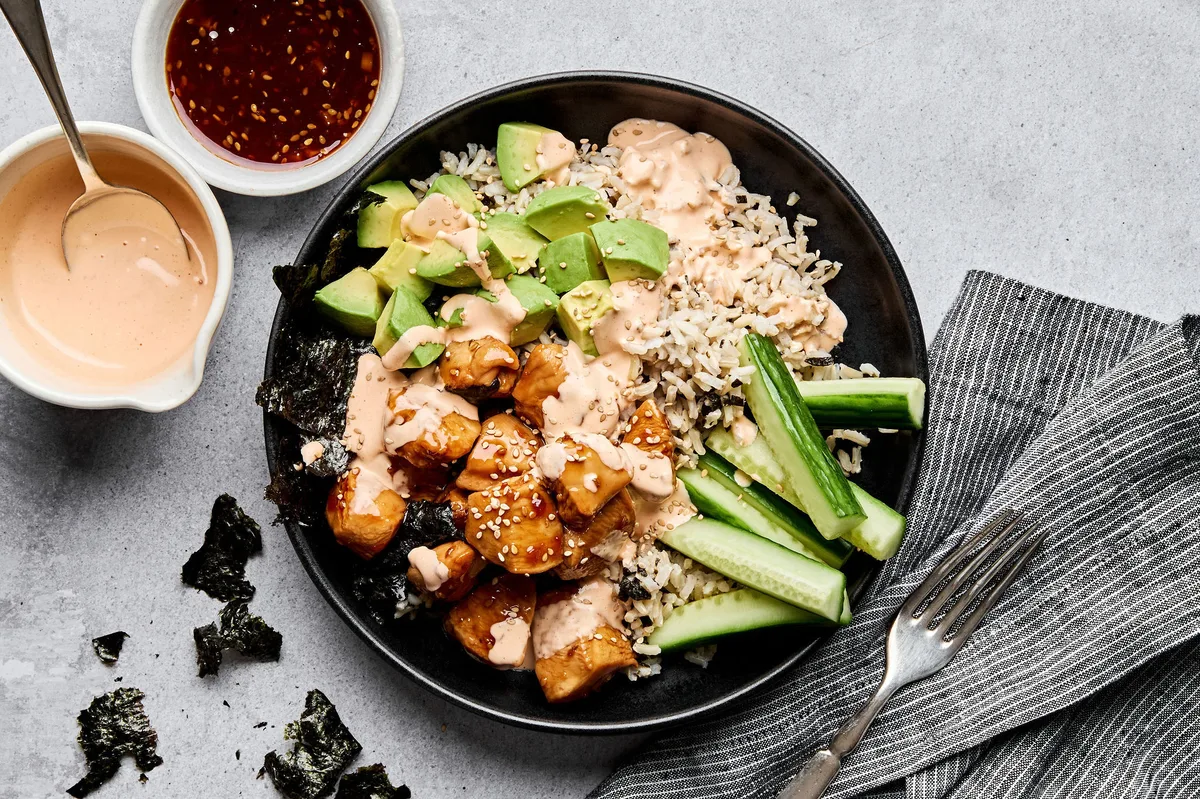 Teriyaki chicken sushi bowl with sriracha mayo, cucumber, avocado and sesame seeds on a bed of seasoned brown rice