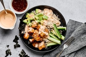 Teriyaki chicken sushi bowl with sriracha mayo, cucumber, avocado and sesame seeds on a bed of seasoned brown rice