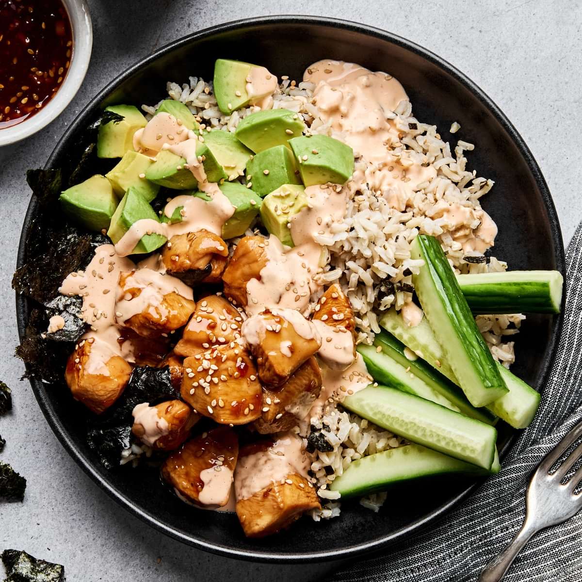 Teriyaki chicken sushi bowl with sriracha mayo, cucumber, avocado and sesame seeds on a bed of seasoned brown rice