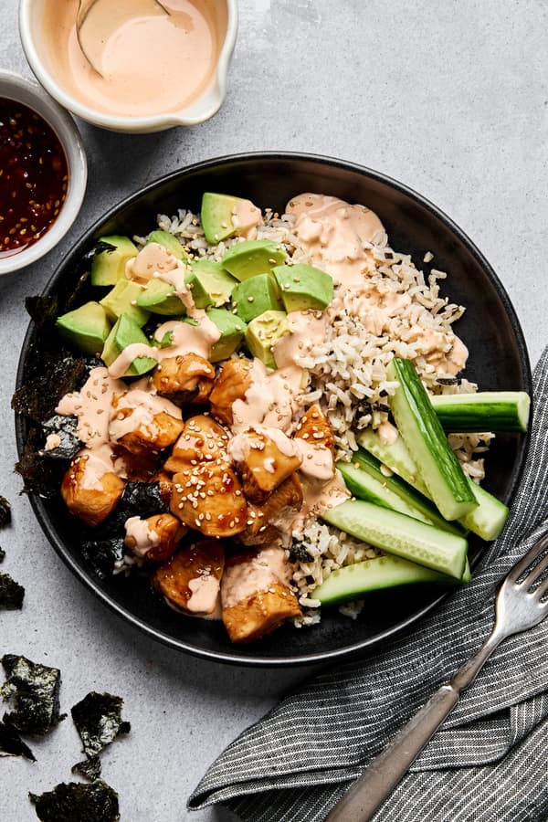 Teriyaki chicken sushi bowl with sriracha mayo, cucumber, avocado and sesame seeds on a bed of seasoned brown rice