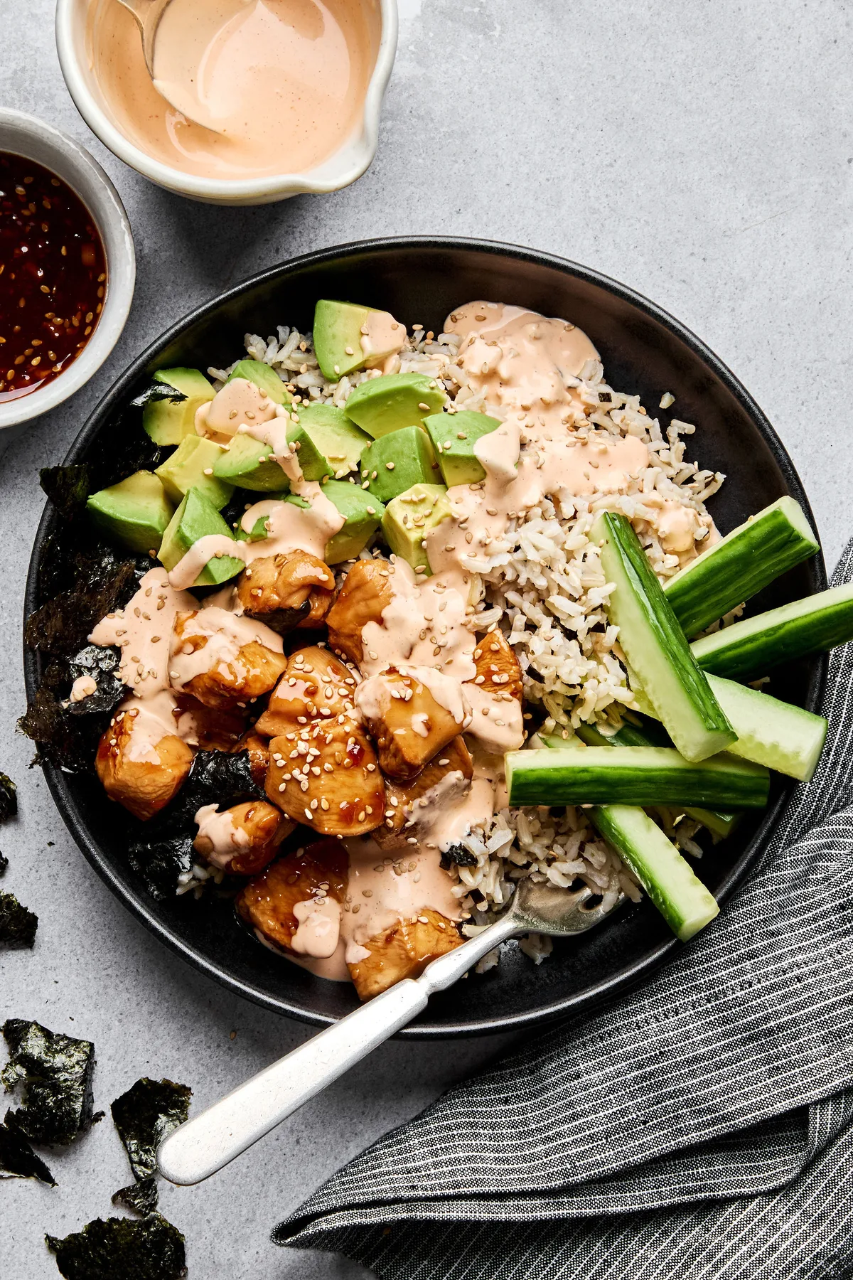 Teriyaki chicken sushi bowl with sriracha mayo, cucumber, avocado and sesame seeds on a bed of seasoned brown rice