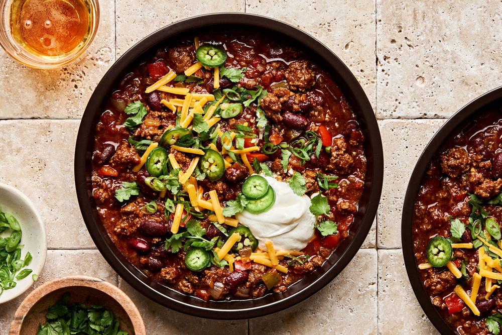 a bowl of Chili Con Carne topped with cilantro, green onion, sour cream, cheese and jalapeno