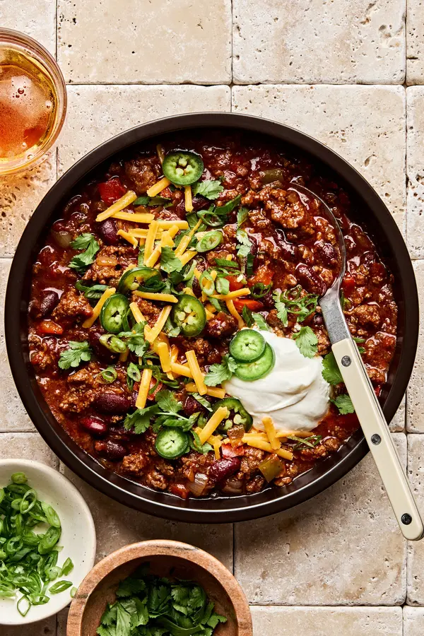 a bowl of Chili Con Carne topped with cilantro, green onion, sour cream, cheese and jalapeno
