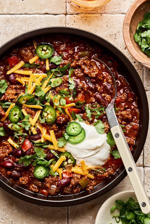 a bowl of Chili Con Carne topped with cilantro, green onion, sour cream, cheese and jalapeno