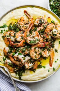 A plate with creamy polenta and chimichurri marinated shrimp with a serving spoon